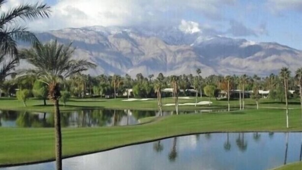 A golf course with a lake, palm trees, and mountains in the background.