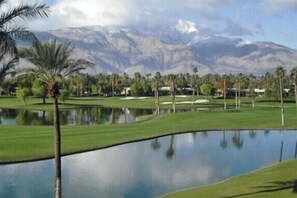 Ein Golfplatz mit See, Palmen und Bergen im Hintergrund.