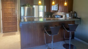 A modern kitchen with a central island, bar stools, stainless steel appliances, and pendant lighting.