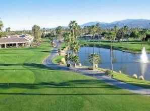Un parcours de golf avec un étang, des palmiers et un bâtiment en arrière-plan.