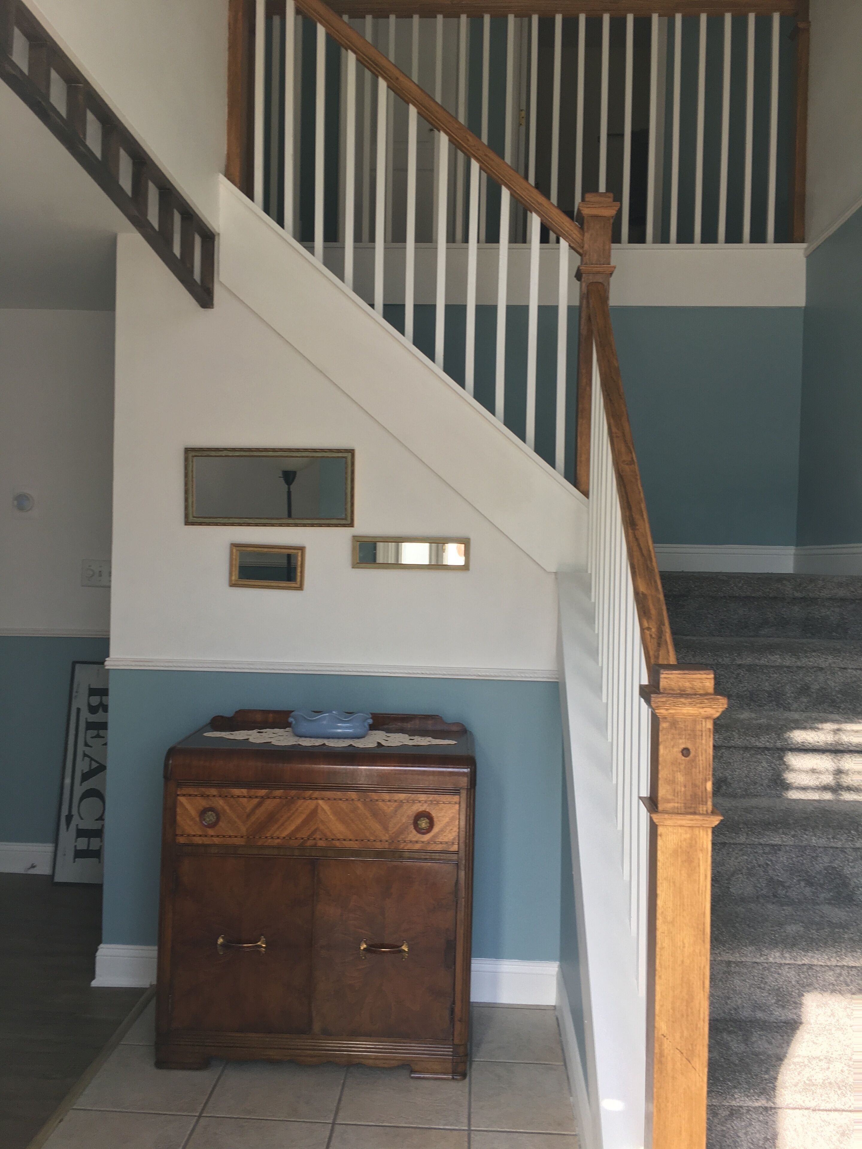 Una escalera con barandillas de madera y balaustradas blancas, que conduce a un rellano con una pared azul y un armario de madera con cajones.