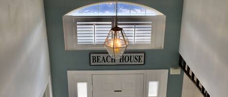 Una escalera conduce a una puerta con la leyenda "BEACH HOUSE", con veleros arriba y una lámpara colgante.