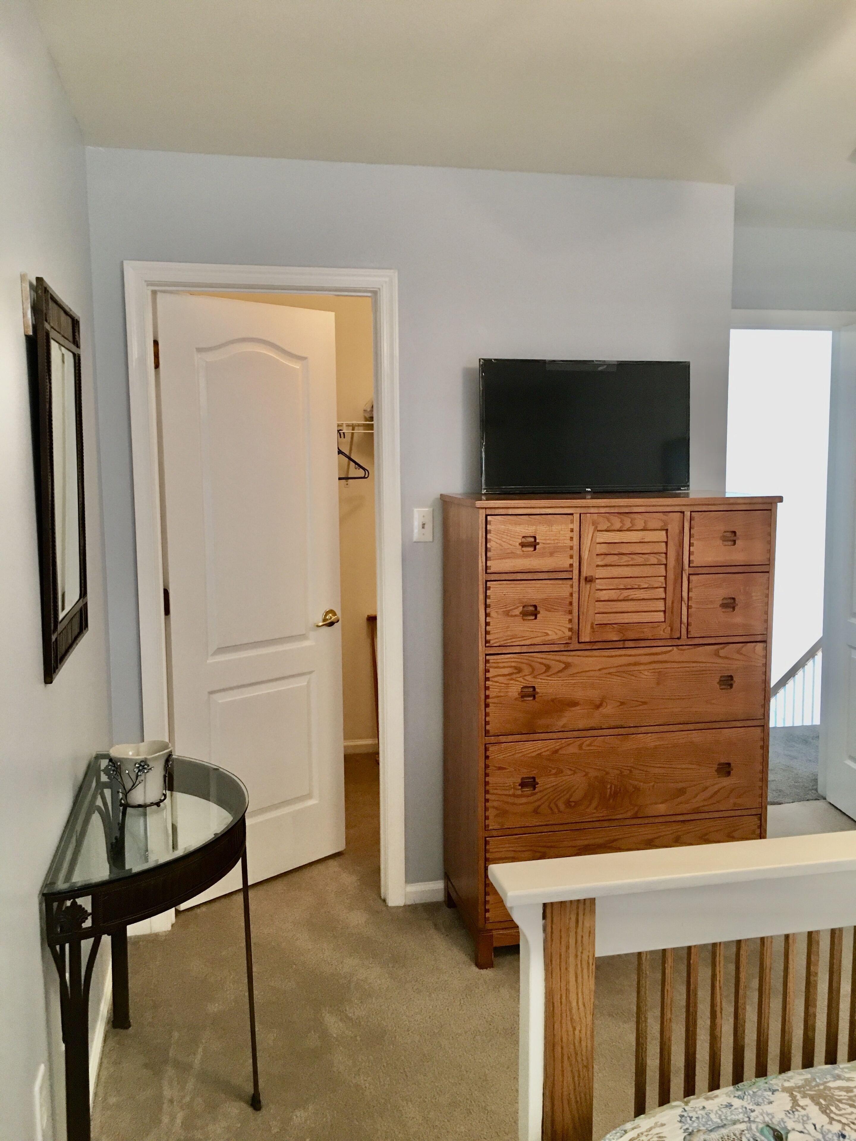 Una habitación con un aparador de madera, un televisor encima, una mesa de vidrio y una puerta que da a otra habitación.