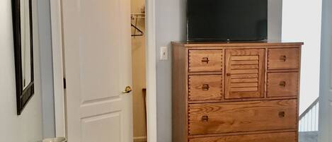 Una habitación con un aparador de madera, un televisor encima, una mesa de vidrio y una puerta que da a otra habitación.