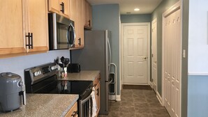 A kitchen with wooden cabinets, a stainless steel microwave, a black stove, and a refrigerator. - Rehoboth Beach-Luxury Villa-Linens Included (Rehoboth Beach)