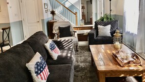 A living room with a dark-colored sofa, a wooden coffee table, and a staircase leading to an upper floor. - Rehoboth Beach-Luxury Villa-Linens Included (Rehoboth Beach)