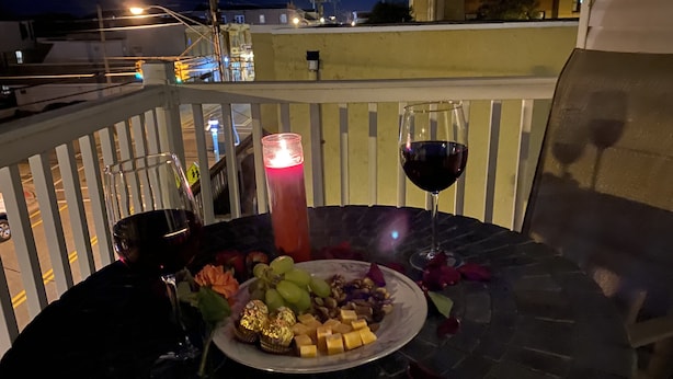A table set with a plate of cheese, grapes, and nuts, two glasses of wine, and a lit candle on a balcony at night. - NEW! Corner Townhouse: 3BR, 2 balcony home, 2 blocks to beach! (Wildwood)