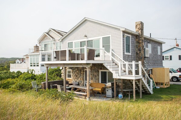 Une maison à deux étages avec un balcon, une cheminée en pierre et une terrasse en bois.