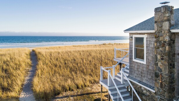 A coastal building with a stone exterior and a wooden deck leading to a beach.