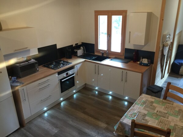 A compact kitchen with white cabinets, a microwave, a stove, and a sink. There is a window above the sink and a table with a tablecloth.