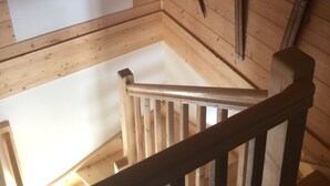 Un interior de madera con techo blanco, una escalera de madera y un martillo apoyado en la pared.