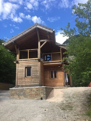 Une cabane en bois avec des fondations en pierre, un balcon et une vue sur la forêt environnante.