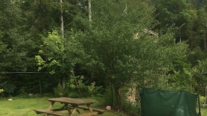 Una mesa de picnic en un área verde con una estructura de malla verde y árboles al fondo.