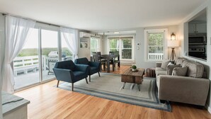 A spacious living room with a wooden floor, a dining area, and a large sliding glass door leading to a deck.