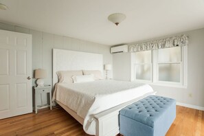 A bedroom with a bed, bedside lamps, a window with curtains, a white door, and a blue bench.