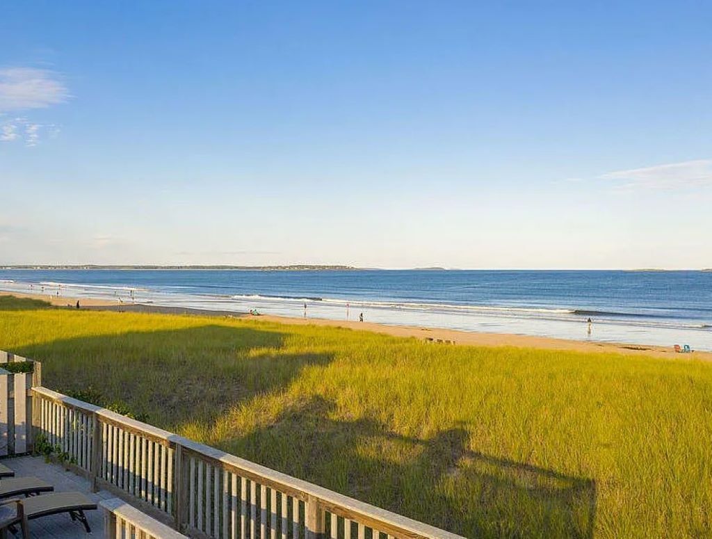 A beach view with a wooden deck and grassy area in the foreground.