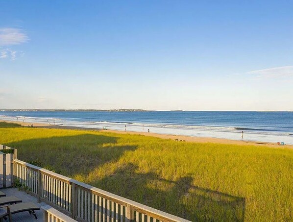 A beach view with a wooden deck and grassy area in the foreground.