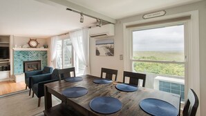 A dining area with a wooden table, blue placemats, and chairs. There is a view of the outdoors through a large window.