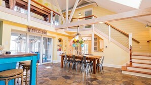 A spacious interior with a central dining area, a bar with stools, and a staircase leading to an upper level.