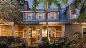 A two-story house with a covered porch, a brick pathway, and a palm tree.
