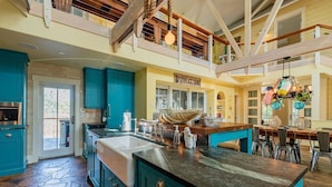 A spacious kitchen with teal cabinets, a large island, and a stone floor.