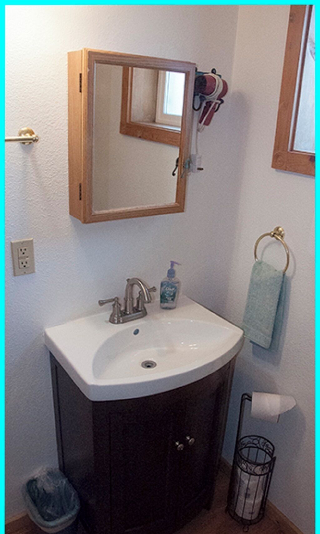Un baño con un lavabo blanco, un mueble oscuro y un espejo encima.