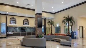 Um hall amplo com um sofá cinza curvo, um balcão de recepção, um pilar grande e uma palmeira.