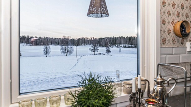 Una finestra con vista su un paesaggio innevato, un lampadario a sospensione e oggetti da cucina sul davanzale.