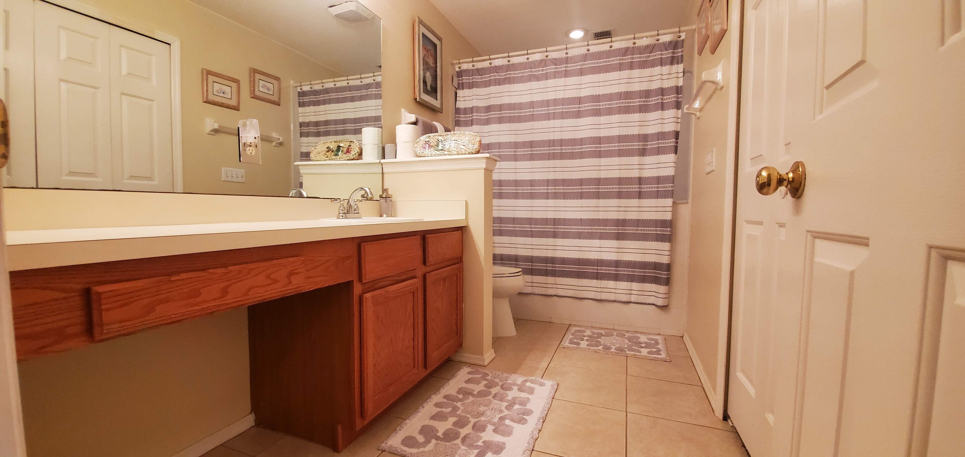 A bathroom with a wooden vanity, a sink, a toilet, and a shower curtain.