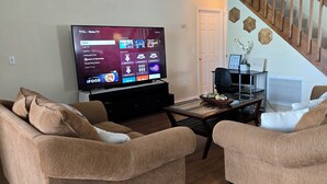 Ett vardagsrum med en platt-TV, två bruna soffor, ett soffbord och en trappa i bakgrunden.
