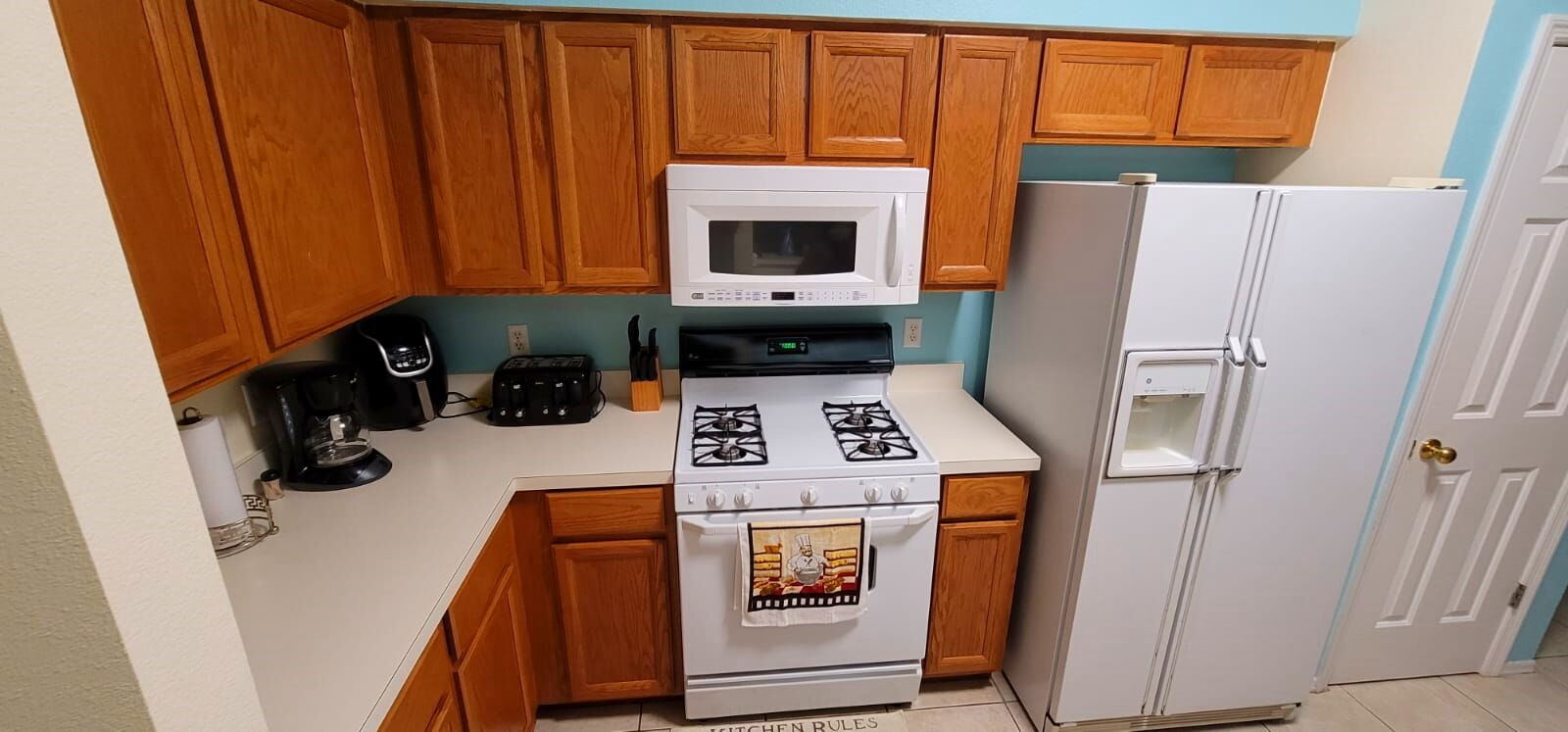 Une cuisine compacte avec des meubles en bois, une cuisinière blanche, un four à micro-ondes, une machine à café et un réfrigérateur.