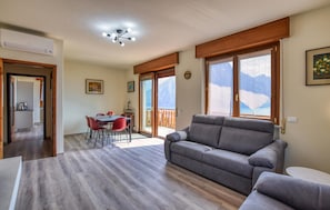 Un salon avec un canapé gris, un coin repas avec des chaises rouges et de grandes fenêtres offrant une vue sur les montagnes.
