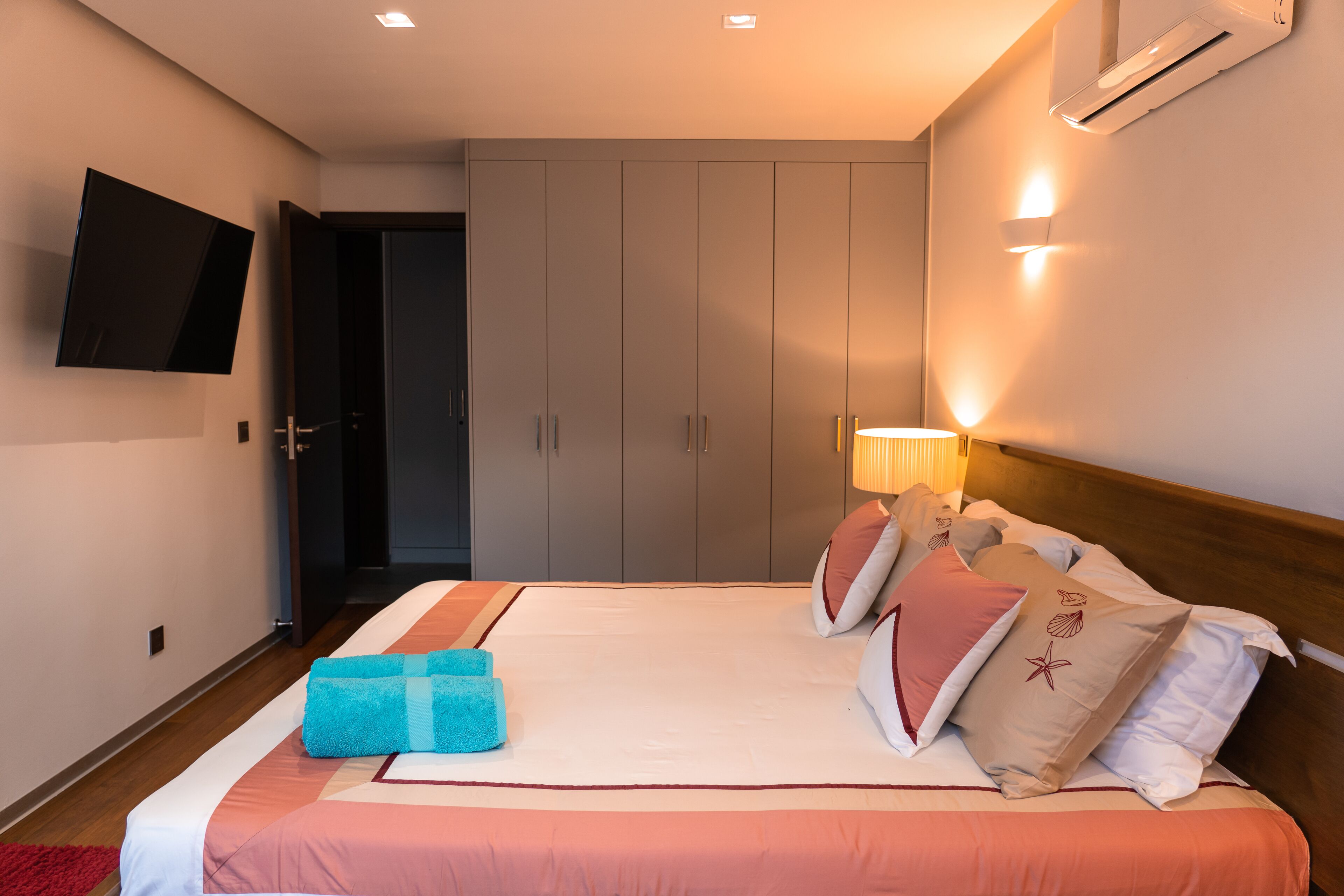 Une chambre d’hôtel avec un lit, un téléviseur fixé au mur et une porte donnant sur une autre pièce.