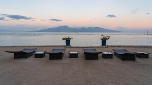 A beachside lounge area with lounge chairs and tables, overlooking a calm sea with distant mountains. - Villa Jessivia Beach (Moorea-Maiao)