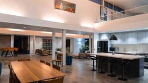 A spacious open-plan living area with a dining table, bar stools, and a kitchen area with a large island. - Villa Jessivia Beach (Moorea-Maiao)