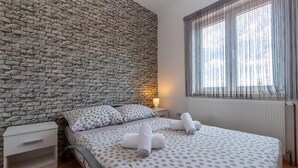 A bedroom with a brick wall, a bed with polka dot bedding, a nightstand, a lamp, and a window with sheer curtains. - Lovely home in Pridraga (Pridraga)