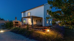 A two-story house with a covered patio area, a stone fireplace, and a well-lit outdoor space. - Lovely home in Pridraga (Pridraga)