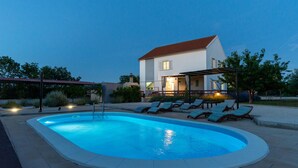 A swimming pool with lounge chairs, a covered patio, and a house in the background. - Lovely home in Pridraga (Pridraga)