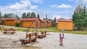 Eine Reihe von Holzhäuschen mit roten Dächern, eine Holzschaukel und ein Sandkasten mit Ball und Wippe.