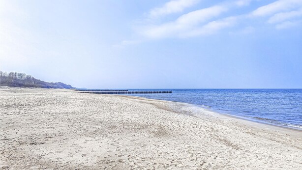 Ein Strand mit einem Steg, der ins Wasser ragt, sandigem Untergrund und einem klaren Himmel.