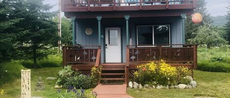 A two-story building with a balcony, a front door, and a small garden with a pathway leading to the entrance.
