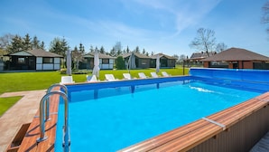A swimming pool with a wooden deck, lounge chairs, and a clear blue sky. - Beautiful home in Postomino (Postomino)