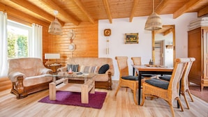A cozy log cabin interior with a wooden ceiling, a sofa, a dining table with chairs, and a large mirror. - Beautiful home in Postomino (Postomino)
