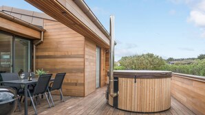 Een houten terras met een jacuzzi, een tafel met stoelen en een glazen deur naar een kamer.