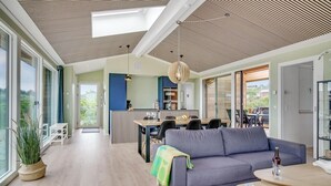 Een moderne woonkamer met een grijze bank, een eethoek met tafel en stoelen, en een keuken op de achtergrond.