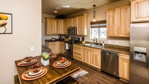 Een moderne keuken met houten kastjes, roestvrijstalen apparatuur en een eethoek met een houten tafel en koperen servies.