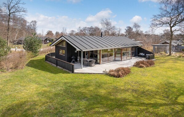 Ein modernes Haus mit einer großen Terrasse, einer überdachten Veranda und einem Metalldach.