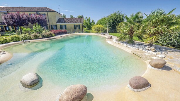 Une piscine aux eaux cristallines, bordée de sable, entourée de rochers et de palmiers.
