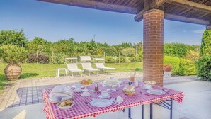 Un espace extérieur aménagé pour les repas, avec une nappe à carreaux, des chaises blanches et un pilier en briques.