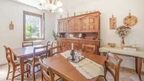 Un coin repas avec une table et des chaises en bois, un lustre et une fenêtre donnant sur un paysage verdoyant.
